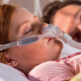 Photograph of a woman sleeping on her side wearing the Nuance Pro with her partner behind her