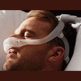 Man asleep on his side in bed wearing the DreamWear nasal mask with the tube running overhead