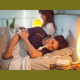 Photograph of a man sleeping on his side wearing the AirFit P10 mask, with the AirMini machine on the nightstand