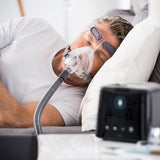 Photograph of a man sleeping on his side wearing the Simplus full face mask, connected to a CPAP machine on the nightstand
