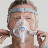 Photograph of a man fitting the Vitera full face mask, holding the lower headgear clips at each cheek