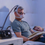 Photograph of a man reading in bed wearing the AirFit F30i while his partner sleeps beside him