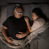 Man asleep on his back in bed wearing the AirFit N30i, with his partner asleep beside him