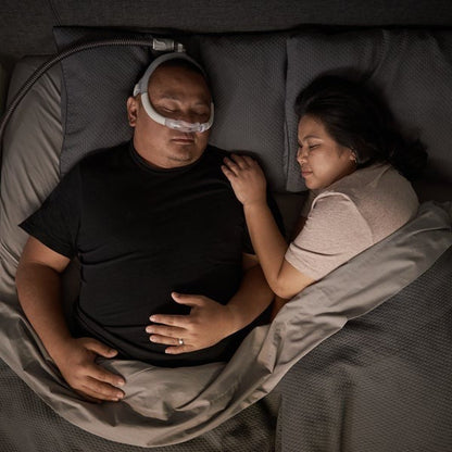 Man asleep on his back in bed wearing the AirFit N30i, with his partner asleep beside him