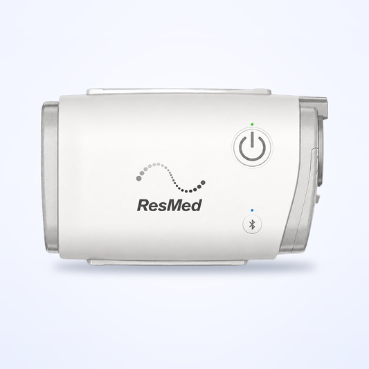 ResMed AirMini travel CPAP machine on a soft blue background, power button and Bluetooth indicator visible