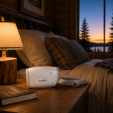 The ResMed AirMini and its tubing rest on a cabin nightstand beside a lamp, a sunset through the window