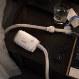 ResMed AirMini machine and tube on a bedside nightstand at night, with glasses and a water glass nearby