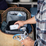A man packs the ResMed AirMini, its tubing and a mask into a padded travel bag in a car trunk