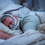 Photograph of a man asleep in bed wearing the AirTouch F30i Comfort with its grey fabric-covered frame