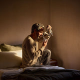Photograph of a man sitting on the edge of his bed in warm light, putting on the AirTouch F40