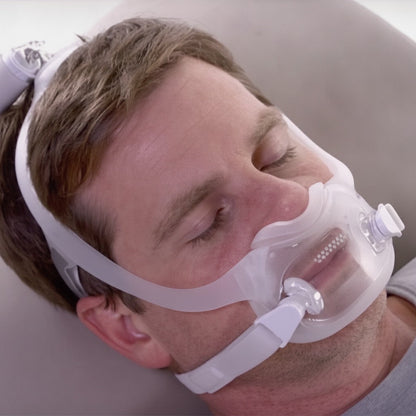 Man asleep on his side wearing the DreamWear Full Face mask, with the tube running up from the top of his head