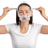 Photograph of a woman wearing the AirFit F30i and drawing the upper headgear strap back across her head