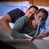 Photograph of a couple asleep in bed, the woman wearing the AirFit F40 as her partner holds her