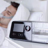 A man sleeps in a nasal pillow mask beside the React Health Luna G3 sitting on a bedside table