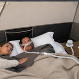 A couple asleep in a tent, the man wearing a nasal pillow mask connected to the Transcend Micro